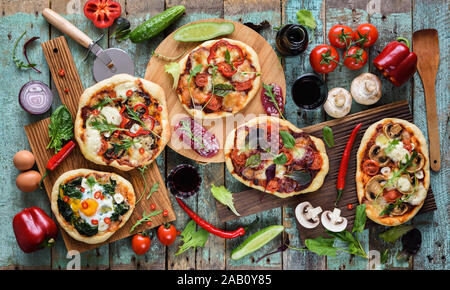 Flatlay frisch prerared köstliche italienische Pizza. Fünf Pizzas mit Eier, Salami, Pilze und Gemüse serviert mit Rohstoffen und Re Stockfoto