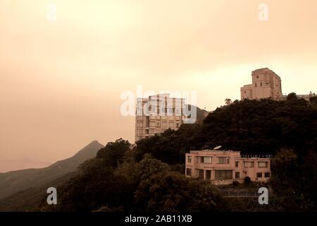 Ein paar vereinzelte Häuser auf dem Hügel, die von Victoria Peak in Hongkong, China bei Sonnenuntergang geschossen wurden. Stockfoto