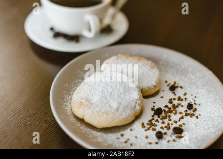 Käsekuchen mit Puderzucker auf einem Schild auf dem Hintergrund von frisch gebrühtem Kaffee. Falsche leckeren süßen Zucker Frühstück. Stockfoto