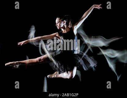 Eine kaukasische junge Frau ballerina Tänzerin tanzen auf schwarzen Hintergrund mit Licht malen motion blur-Effekt isoliert Stockfoto