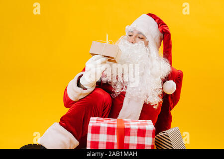 Santa Claus auf dem Boden sitzend, ein kleines Geschenk in der Hand Stockfoto