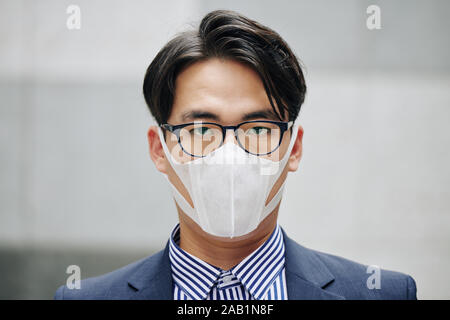 Angesichts der schwerwiegenden Asiatische Geschäftsmann das Tragen schützender Maske in Stadt mit Luftverschmutzung Stockfoto