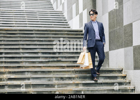 Stilvolle hübscher junger Mann in Anzug zu Fuß die Treppen mit Shopping-bag Stockfoto