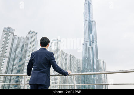 Rückansicht der ehrgeizige Unternehmer mit modernen Wolkenkratzern und genießen Blick auf die Stadt suchen Stockfoto