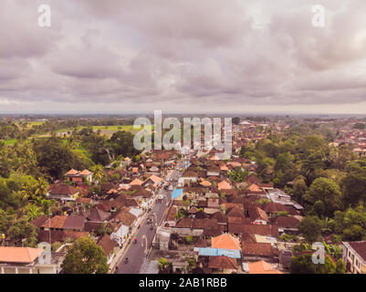 Viele Villen mit braun-orange Schindeldächer zwischen tropischen Bäumen am Himmel Hintergrund in Ubud auf Bali. Sonne scheint auf Sie. Antenne horizontal Stockfoto