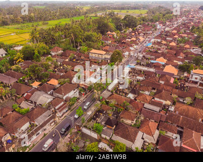 Viele Villen mit braun-orange Schindeldächer zwischen tropischen Bäumen am Himmel Hintergrund in Ubud auf Bali. Sonne scheint auf Sie. Antenne horizontal Stockfoto