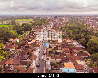 Viele Villen mit braun-orange Schindeldächer zwischen tropischen Bäumen am Himmel Hintergrund in Ubud auf Bali. Sonne scheint auf Sie. Antenne horizontal Stockfoto