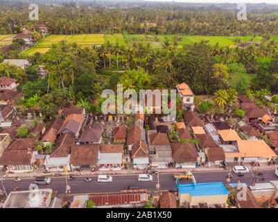 Viele Villen mit braun-orange Schindeldächer zwischen tropischen Bäumen am Himmel Hintergrund in Ubud auf Bali. Sonne scheint auf Sie. Antenne horizontal Stockfoto