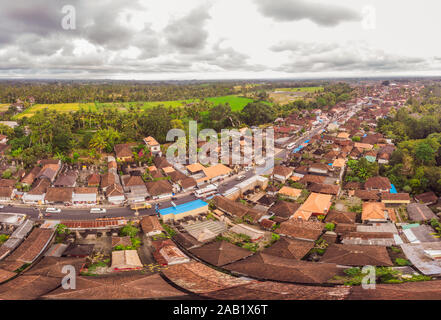 Viele Villen mit braun-orange Schindeldächer zwischen tropischen Bäumen am Himmel Hintergrund in Ubud auf Bali. Sonne scheint auf Sie. Antenne horizontal Stockfoto