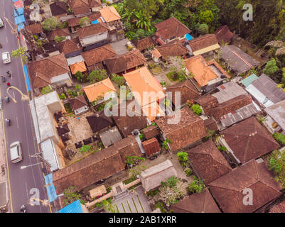 Viele Villen mit braun-orange Schindeldächer zwischen tropischen Bäumen am Himmel Hintergrund in Ubud auf Bali. Sonne scheint auf Sie. Antenne horizontal Stockfoto