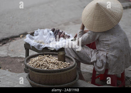 Eine strasse Erdnuss Trader sitzt auf einer Bank vor einem improvisierten Zähler. Vietnam. Stockfoto