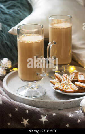 Hausgemachte Latte in Glas Tassen, serviert mit Lebkuchen auf dem Hintergrund der Plaid, Kissen und Girlanden. Stockfoto