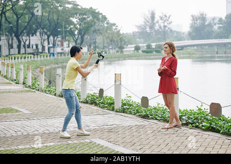 Zwei weibliche Freunde Aufnehmen von Videos auf dem Smartphone auf Bank von City River Stockfoto