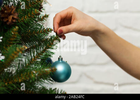 Weibliche Hand hängt eine schöne blaue Kugel auf einem Merry Christmas Tree. Nahaufnahme Stockfoto