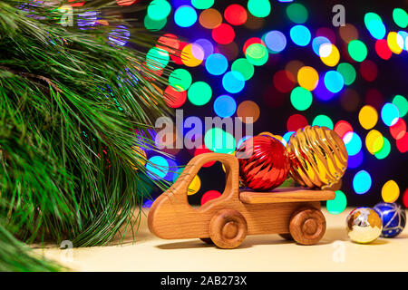 Close-up aus Holz Spielzeug-LKW brachten bunten Weihnachtskugeln zu einem Weihnachtsbaum auf dem Hintergrund der vielen bunten Lichtern. Bild für das Neue Jahr desi Stockfoto