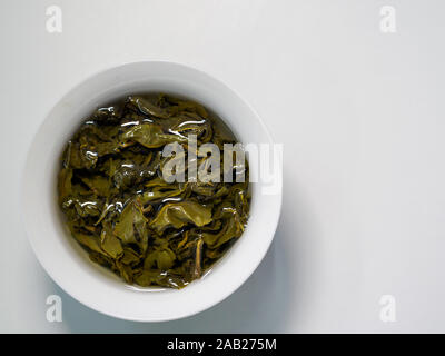 Flach Sicht der Chinesischen grünen Oolong Tee Blätter in einer Porzellantasse/gaiwan gegen einen weißen Hintergrund mit Kopie Raum gebraut Stockfoto