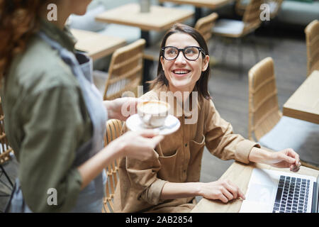 Hohen winkel Porträt der jungen Frau an der Kellnerin Lächeln bringen Kaffee Tasse während der Arbeit im Cafe, kopieren Raum Stockfoto