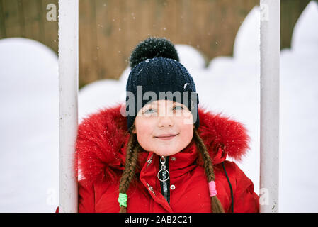 Winter Portrait eines kleinen Mädchens in einen Hut und eine rote Jacke auf einer Schaukel Stockfoto