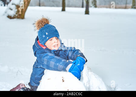 Kleinen Jungen in einen Hut und Handschuhe macht ein Schneemann im Winter Stockfoto