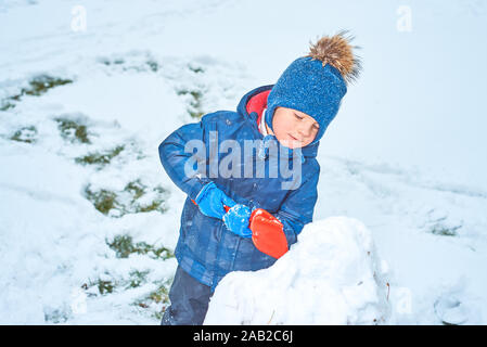 Kleinen Jungen in einen Hut und Handschuhe macht ein Schneemann im Winter Stockfoto