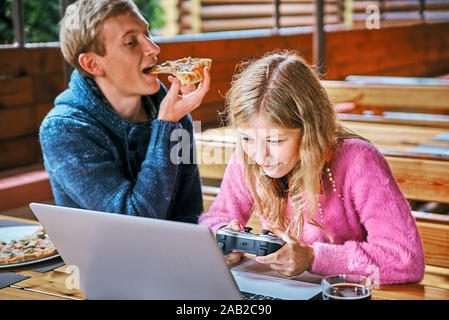 Girl Gamer in einem Cafe mit einem jungen Kerl. Mann essen Pizza Stockfoto