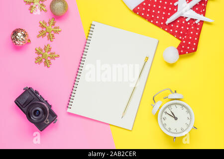 Leerzeichen notebook mockup Weihnachten Travel Concept. Weiße Flugzeug, Santa Hut, Kamera und Weihnachtsdekoration Dekoration auf Gelb und Rosa backgro Stockfoto