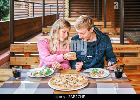 Kerl und ein Mädchen haben das Mittagessen zusammen in einem Café. der Mann und die Frau in ein Restaurant essen. Paar an Smartphone suchen Stockfoto