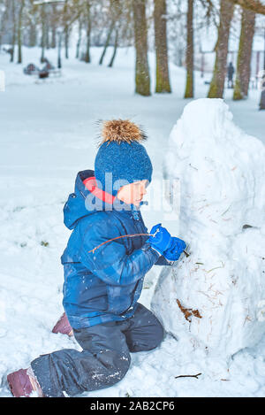 Kleinen Jungen in einen Hut und Handschuhe macht ein Schneemann im Winter Stockfoto