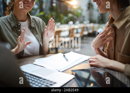 Nahaufnahme des unkenntlich junge Frau aktiv gestikuliert während der Sitzung im Cafe mit weiblichen Partner über Tabelle, kopieren Raum Stockfoto