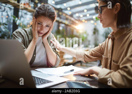 Portrait der frustrierten jungen Frau am Tisch im Cafe mit Freunden oder Kollegen trösteten, Kopie Raum Stockfoto
