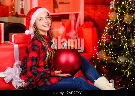 Liebe. Winter Urlaub. Weihnachten Konzept. Kind Lust Santa genießen Feier ins neue Jahr. Kleines süßes Mädchen mit großen Ball Weihnachtsbaum. Geist der Weihnacht. Dekor Shop. Lieblingsfarbe. Red Stil. Stockfoto