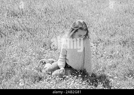 Mädchen zu beruhigen oder traurige Gesicht verbringen Freizeitaktivitäten im Freien. Mädchen sitzt auf Gras an grassplot, grünen Hintergrund. Kind genießen Sie Frühling sonniges Wetter beim Sitzen an der Wiese. Frühling Konzept. Stockfoto