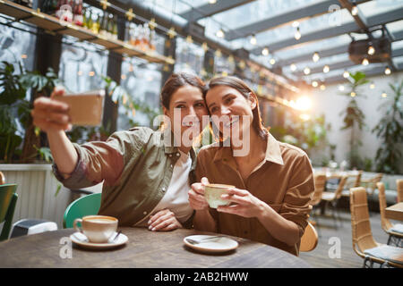 Porträt von zwei Frauen lächelnd an Smartphone Kamera während der Einnahme von selfie Foto im Café im Freien Stockfoto