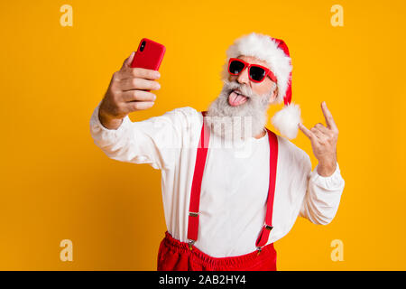 X-mas Party hart. Portrait von funny crazy Santa Claus in Red Hat selfie smart phone Weihnachten Blogger zeigen Hörner Grimasse Zunge heraus tragen Shirt Stockfoto