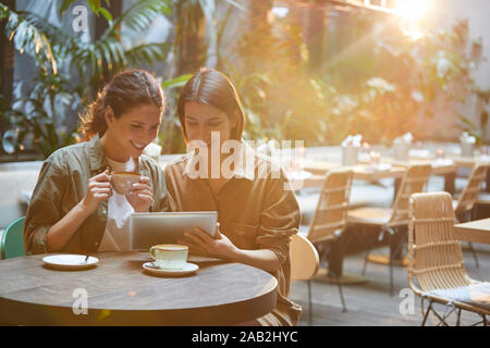 Porträt von zwei zeitgenössischen Frauen an Tablet Bildschirm schaut, während Sie im sonnendurchfluteten care Terrasse, Kopie Raum Stockfoto