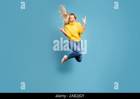 Voller Körper Foto von crazy Lady jumping High Metal Rock Konzert zeigt Hände Hörner aufgeregt Verschleiß gestrickt Gelb pullover Jeans isoliert Blau genießen Stockfoto