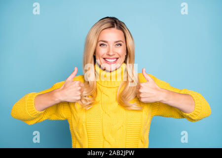 Foto von erstaunlich hübsche blonde Dame heben Daumen bis zum Ausdruck bringen positive Stimmen Haltung neues Produkt tragen Sie warme Pullover gestrickt gelb isoliert Blau Stockfoto