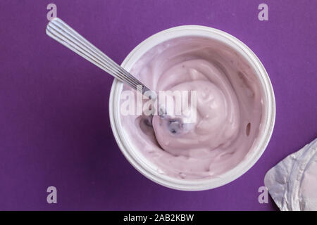 Heidelbeere Joghurt mit Löffel in Schale aus Kunststoff mit Deckel Folie auf der Seite und auf Deep Purple Hintergrund isoliert Stockfoto