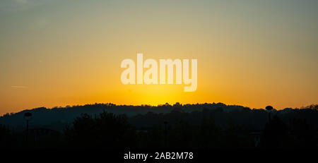 Sonnenuntergang über den Bergen. Hügel bedeckt mit Bäumen, schwarze Silhouette gegen klare Farbe orange Himmel Hintergrund Stockfoto