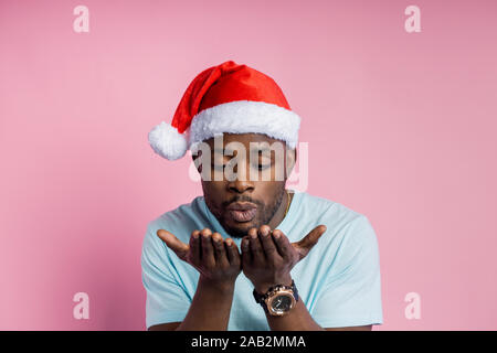 Closeup Schuss attraktive dunkelhäutige Menschen ziehen nach vorne Palmen, blasluft Kiss, tragen, Santa Hut, über Pink Studio Hintergrund posiert. Gefühl c Stockfoto