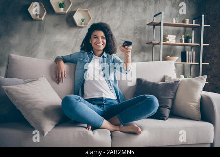 Foto ziemlich dunkle Haut wellig Lady heimelige Stimmung halten TV-Fernbedienung ändern Kanal Suche Favoriten Humor zeigen, sitzen gemütlich Couch lässig Stockfoto