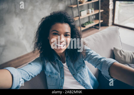 Nahaufnahme der ziemlich lustig dunkle Haut curly blogger Lady, selfies aufgeregt toothy Lächeln social blogger Netzwerk komfortable Sofa casual Denim Stockfoto