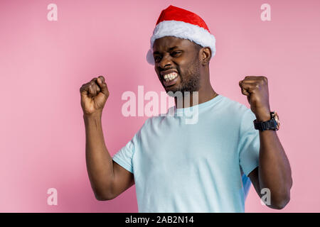 Frustriert, wütend, aggressiv afrikanischer Mann ballte die Fäuste und Zähne, Hände, tragen t-shirt, Santa hat, neben der Suche mit wütenden Ausdruck, p Stockfoto