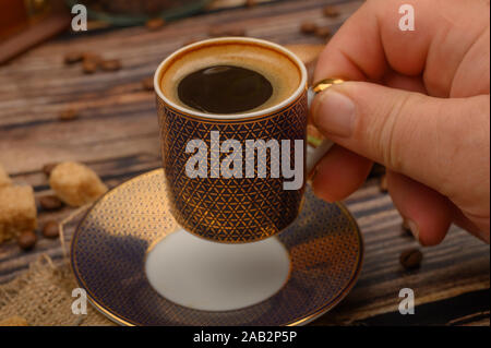 Die Hand des Mädchens hält eine Tasse Kaffee über einen Holztisch mit braunem Zucker und Kaffee Bohnen Stockfoto