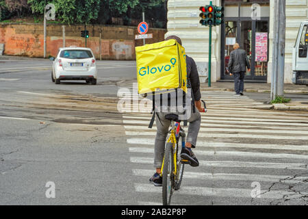 Rom, Italien Glovo On-Demand-Kurierdienst Treiber. Ein Fahrrad Kurier mit quadratischen gelben Rucksack Box mit Firmenlogo auf den Straßen der römischen Hauptstadt Stockfoto