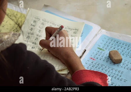 Hart arbeiten. Schulmädchen, die Hausaufgaben im Dorf Nuodeng, Provinz Yunnan, China machen. Stockfoto