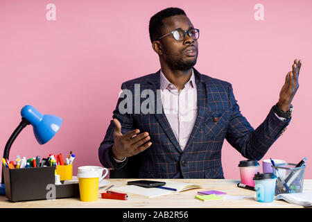 Wütend verwirrt dunkelhäutigen Mann, Inhaber der Firma, wütend Gestik und verständnislos, Verbreitung Hände, sitzen am Schreibtisch, das Tragen von Brillen, Anzug, isol Stockfoto