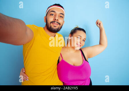 Junge hübsche kaukasischen Paar in helle Kleidung Ausbildung auf blauem Hintergrund Konzept der Sport, menschliche Gefühle, Ausdruck, gesunden Lebensstil, Beziehung, Familie. Die selfie zusammen und umarmen. Stockfoto