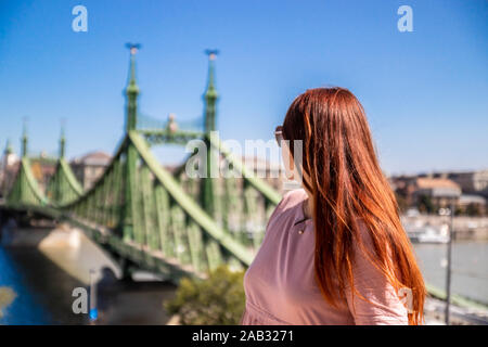 Schöne junge rothaarige Mädchen in einem Sommer Baumwolle Kleid macht ein Foto auf einem Smartphone an einem sonnigen Sommertag in Budapest Stockfoto