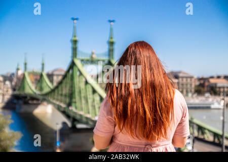 Schöne junge rothaarige Mädchen in einem Sommer Baumwolle Kleid macht ein Foto auf einem Smartphone an einem sonnigen Sommertag in Budapest Stockfoto